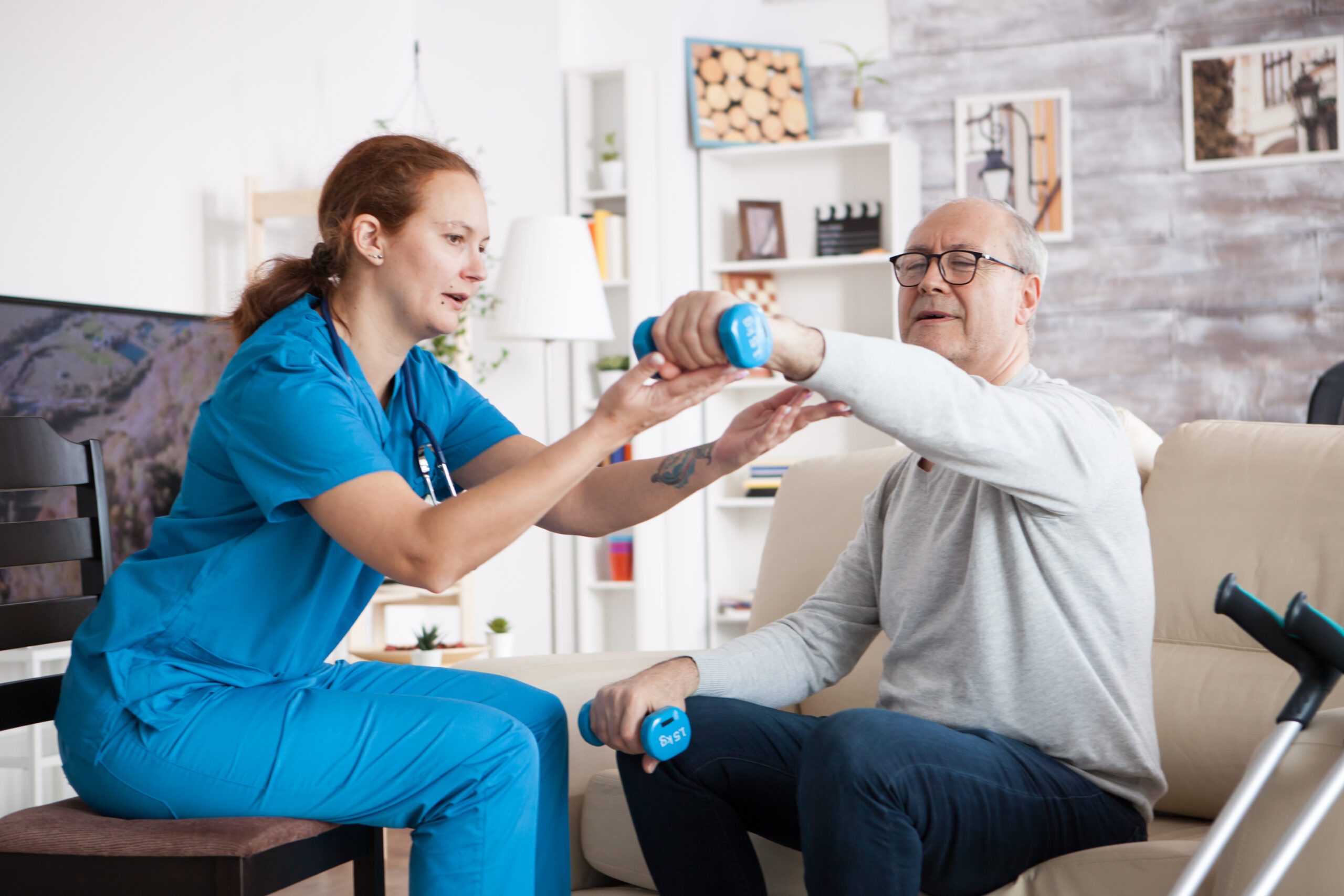 Senior man in nursing home with doing physical therapy with help from nurse using dumbbells.